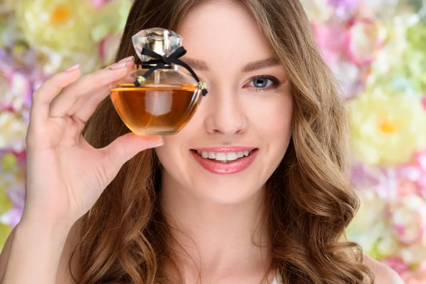 close-up portrait of smiling young woman covering one eye with bottle of perfume