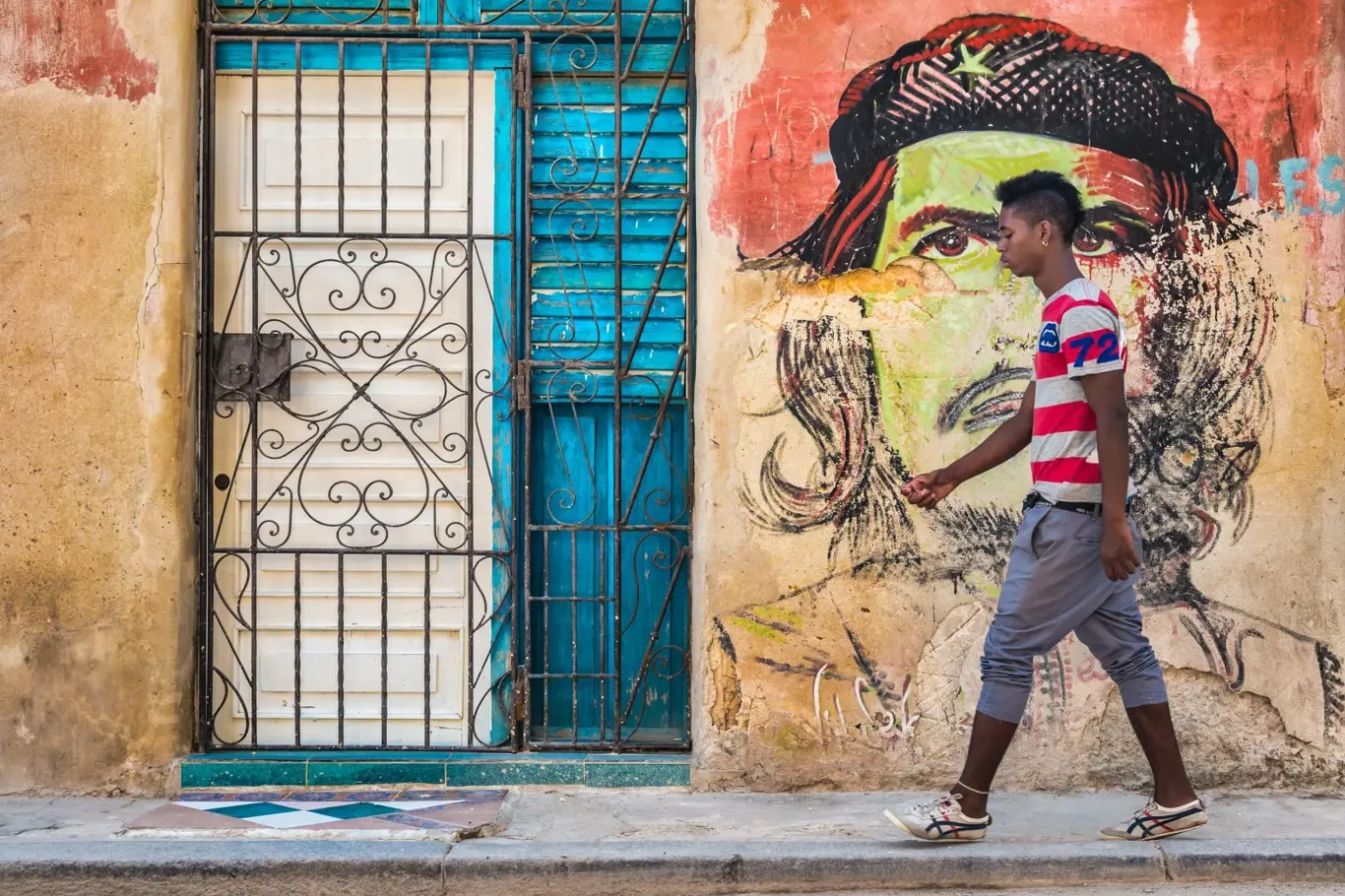 Mladý kubánský muž prochází kolem barevného portrétu Che Guevary namalovaného na omšelé staré zdi ve staré Havaně.