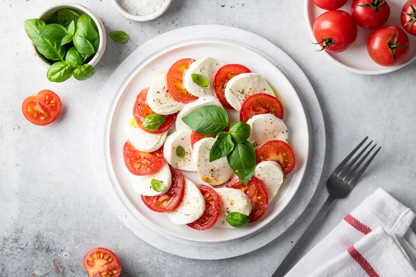 Italian caprese salad with sliced tomatoes, mozzarella, basil, olive oil on a light background. Top view.