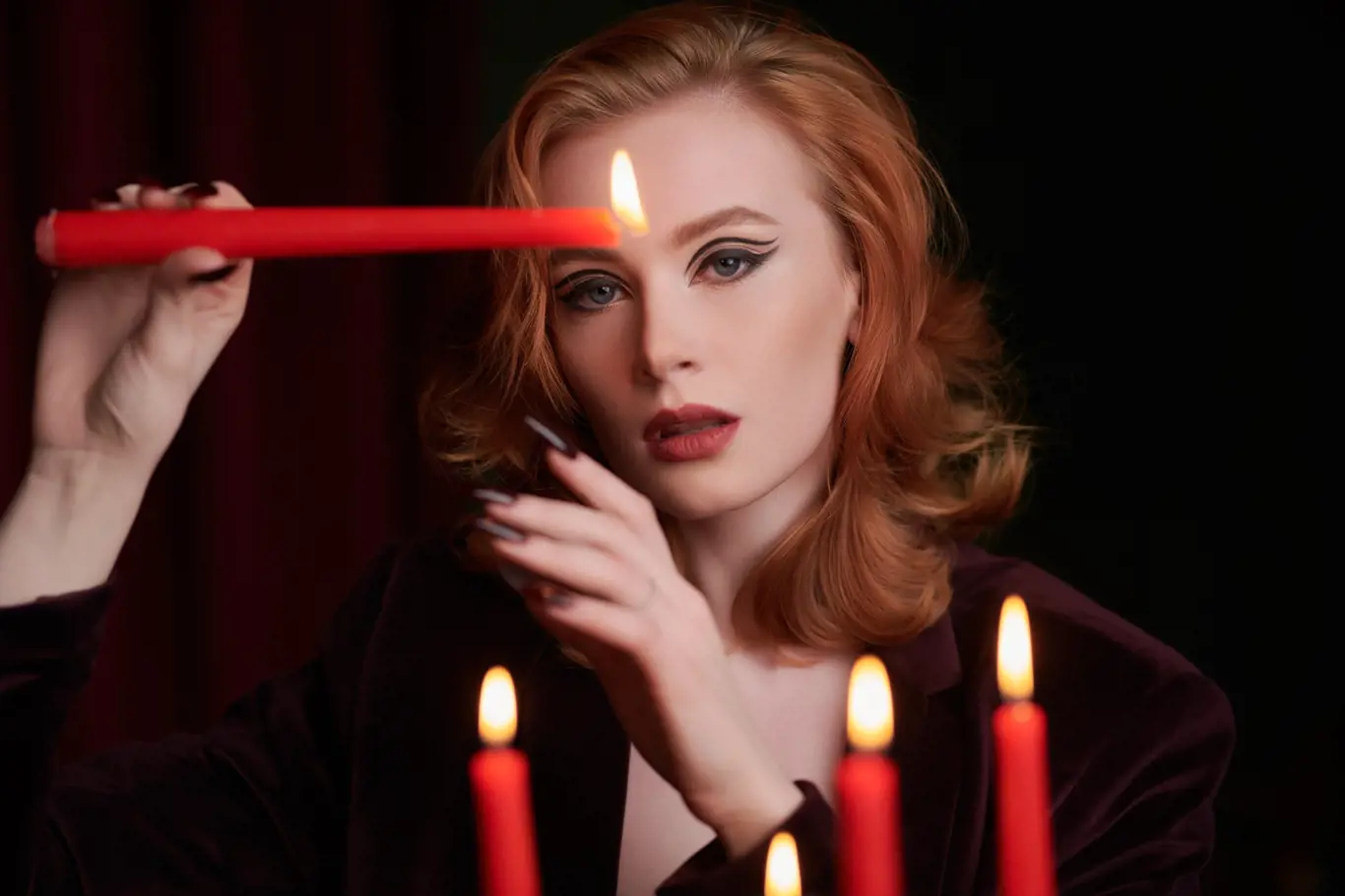 Žena s rudými vlasy drží zapálenou svíčku
