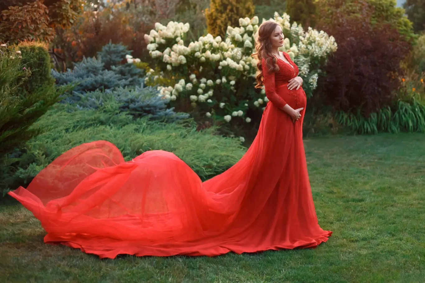 těhotná žena v rudých šatech stojí na zahradě