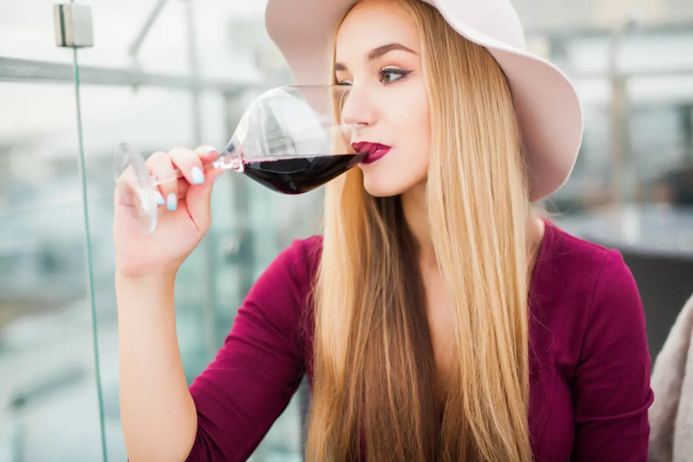 Lovely young woman drinking red wine sitting in a cafe with a great view of the city,hat,trendy outfit girl,nail art,make-up stylist,gold rings