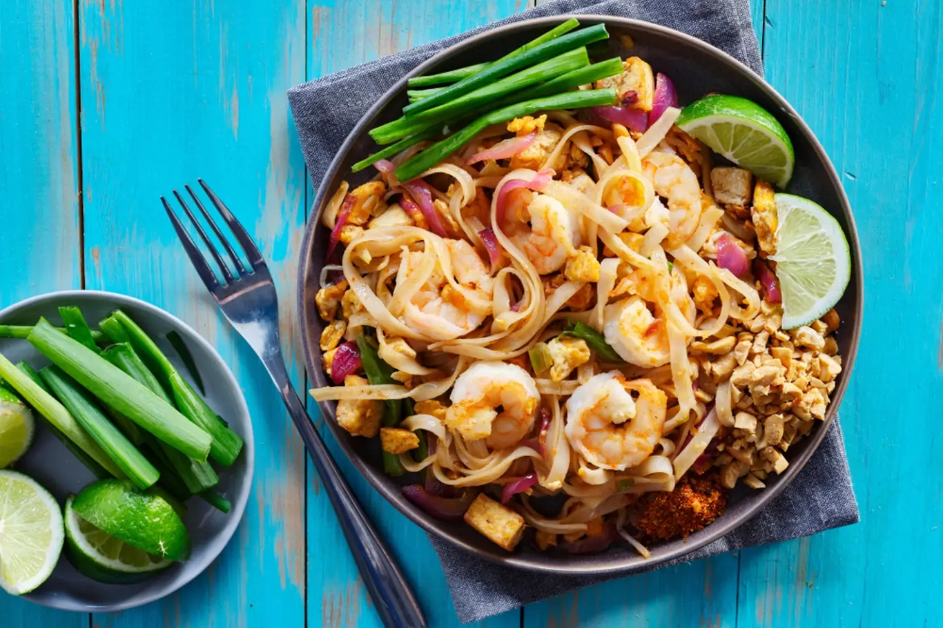 shrimp pad thai on plate in flat lay composition with copy space atop of colorful wooden table