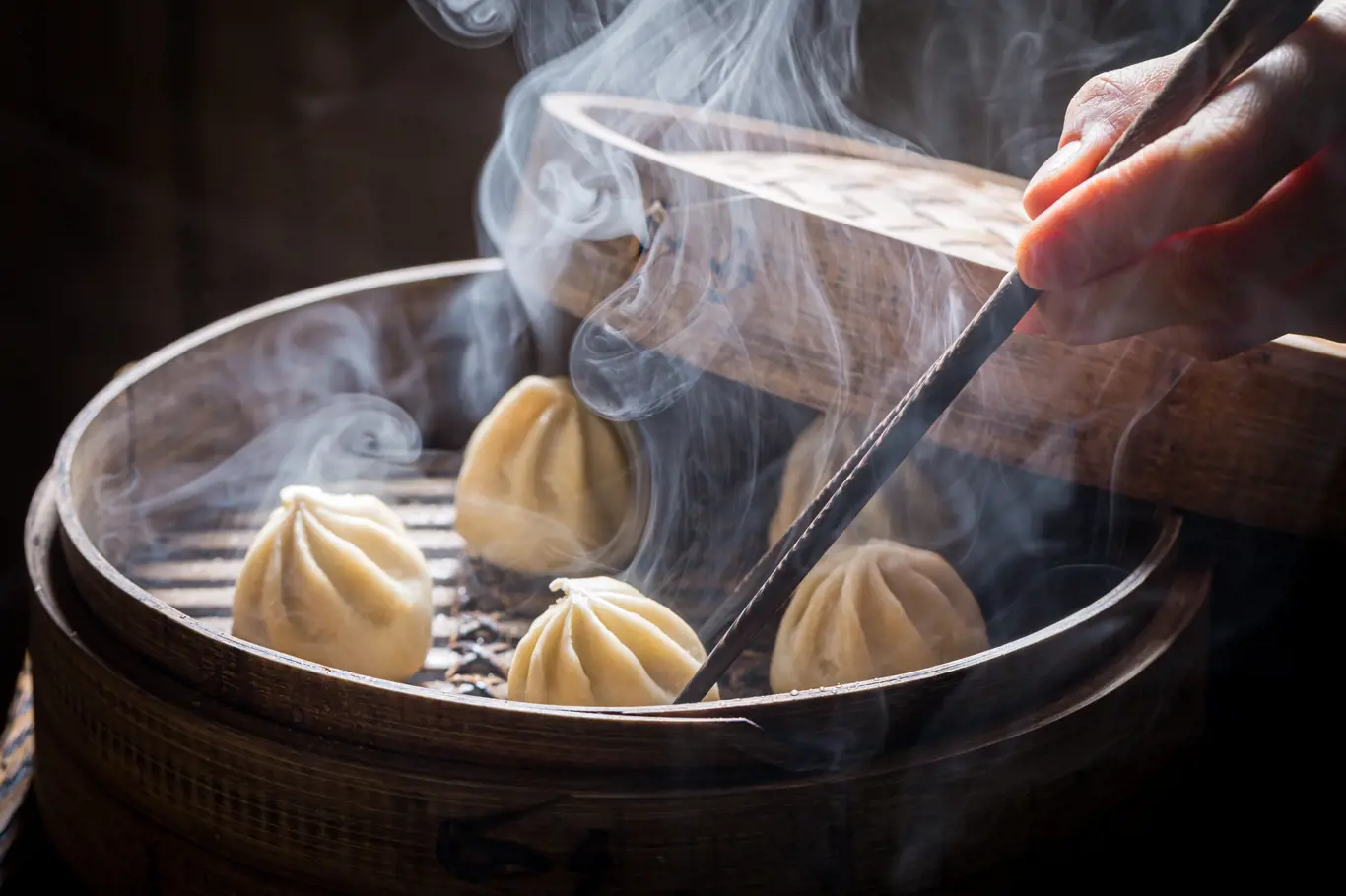 Hot chinese dumplings in wooden steamer on black background. Old Chinese cuisine. 