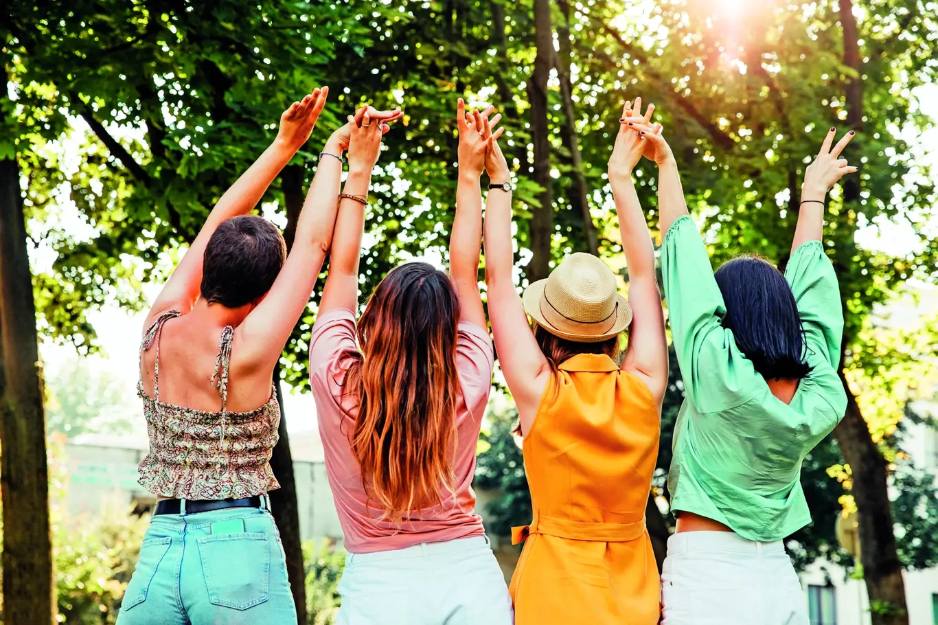 Four young teenage women friends, in a park, holding hands up in the air.