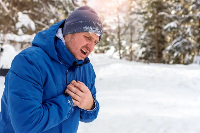 Man with chest pain suffering from heart attack while standing in snowy nature during the day. Shot of a Caucasian man holding chest in pain outdoors. Man holding chest while suffering with heartburn