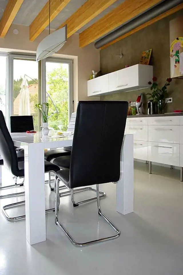Součástí kuchyně je bílý leskle lakovaný jídelní stůl, ke kterému se usedá na pohodlné židle v černé barvě.