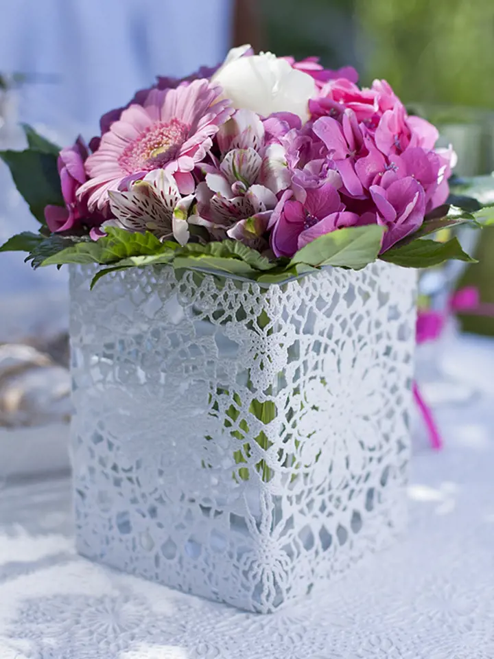 Na první pohled obyčejná skleněná váza se rázem promění v kouzelný originál. Použijte k tomu široký pruh z krajkového ubrusu z PVC. Na slepení obou konců použijte oboustrannou lepicí pásku.