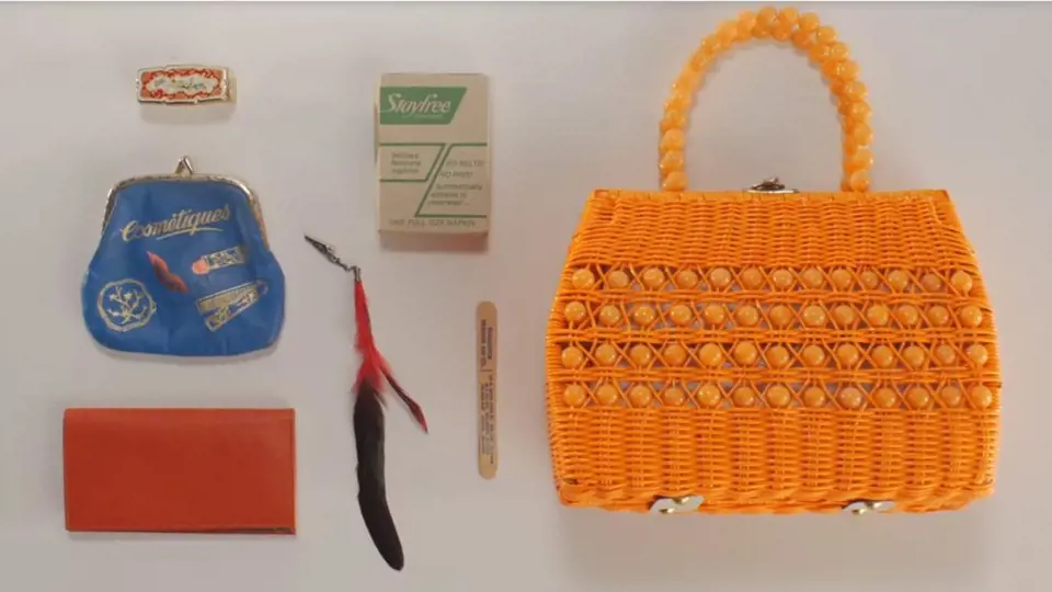 Obsah kabelky z roku 1976 - zrcátko s rtěnkou, pouzdro na make-up, přívěšek, šeková knížka, cigarety a pilníček na nehty