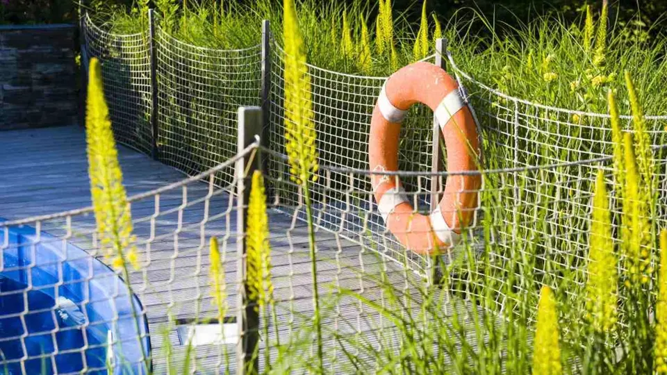 Kvůli malým dětem potřebuje být bazén oplocený. Autor zahrady to řešil vtipně a nápaditě – provazovou sítí.