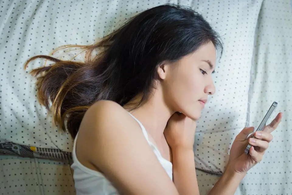 Ilustrační foto - žena odpovídající na SMS v posteli