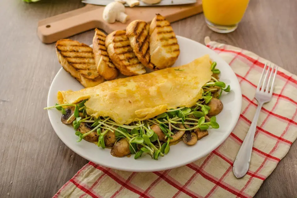 Vaječná omeleta plněná klíčky a hříbky s opečenou bruschettou.