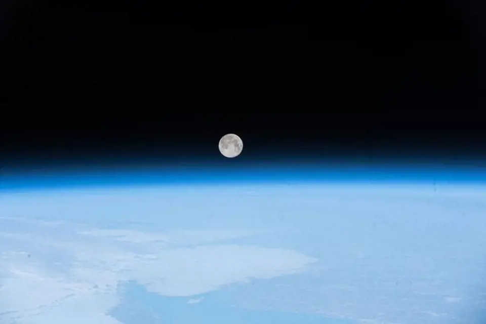 Měsíc, taneční partner Země, vyfotografovaný z Mezinárodní vesmírné stanice vykukuje nad rozostřenou modrou vrstvou atmosféry.