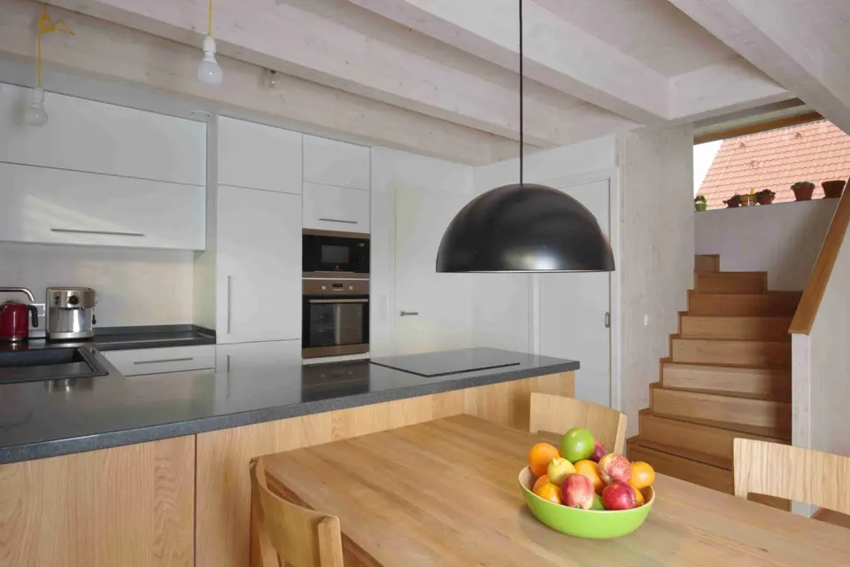 Kuchyň je umístěna dál od velkých prosklených ploch, prosvětluje ji proto bílá barva. Varná deska je záměrně instalována tak, aby ten kdo vaří, měl přehled o zbytku obytného prostoru.