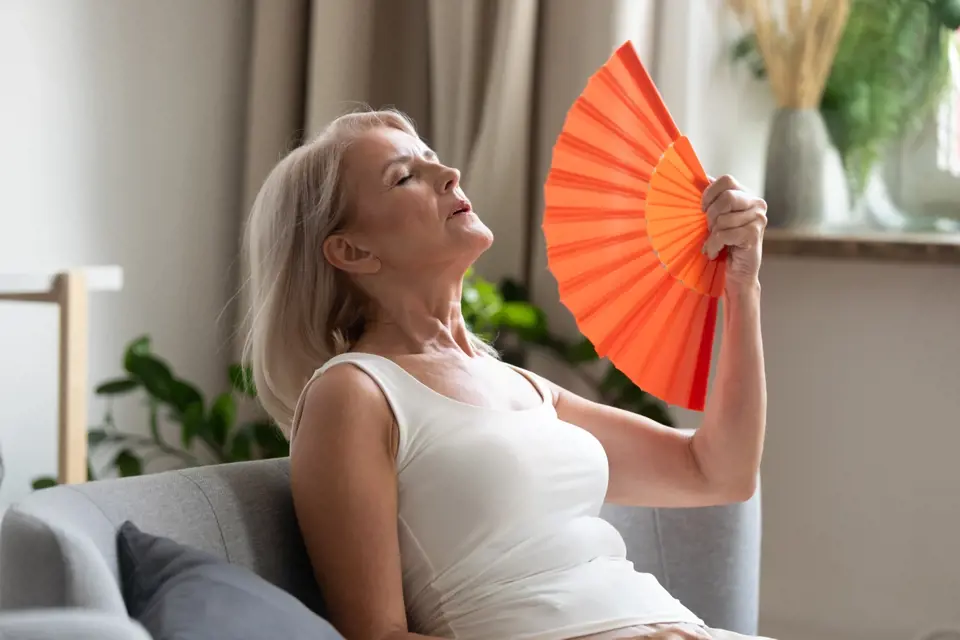 žena ve středním věku se ovívá vějířem kvůli návalům horka