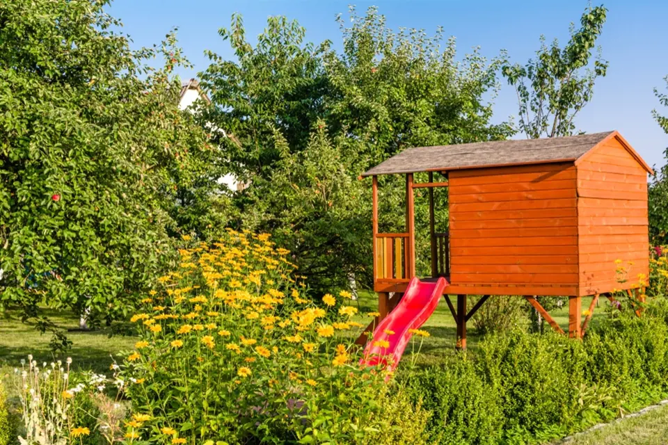 Zahradní domek pro děti doplněný skluzavkou.
